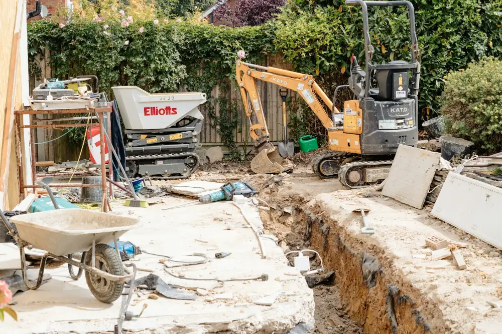 Mini-pelle en train de creuser dans un jardin, première étape du budget piscine enterrée